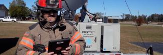 Firefighter using smart device in front of FirstNet deployable tower