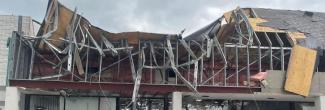 A person looks up at commercial building with the roof and storefront caved in from a tornado in Otsego County