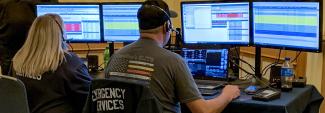 Emergency telecommunicators take calls at a desk with multiple monitors.