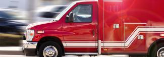 Red ambulance in motion with blurred road in background.