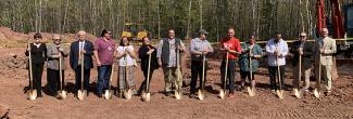 Thirteen people stand with gold shovels, ready to break ground on a cell tower at Red Cliff Reservation