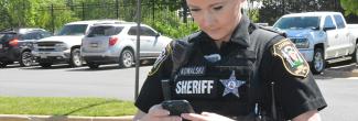 A female Loudon County sheriff in uniform looks down at a phone