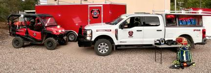 A truck, UTV, and transport trailer outfitted with FirstNet devices such as HPUE parked outside a Northwest Fire and Rescue station. 